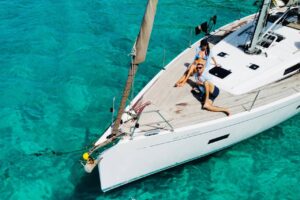 Couple relaxing on the bow of a small group sailing boat trip in Morro Jable over clear turquoise water, Fuerteventura