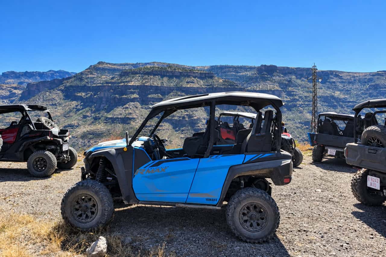 Blue four-seat buggy parked with other off-road vehicles at a mountain stop in Gran Canaria, surrounded by rugged volcanic scenery.