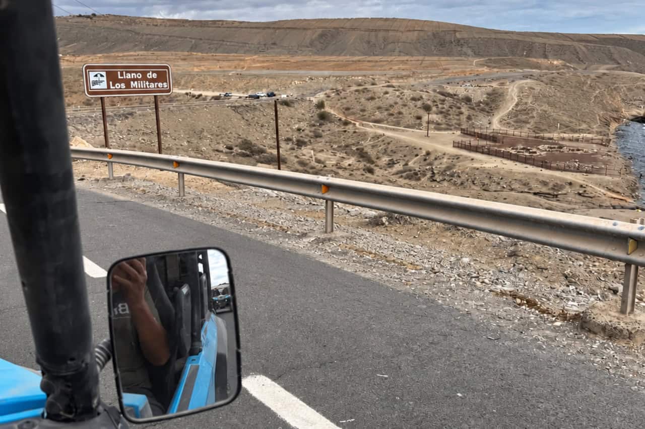 View from a buggy beside the Llano de Los Militares sign in Gran Canaria, showing the dry volcanic landscape and roads used during the adventure.