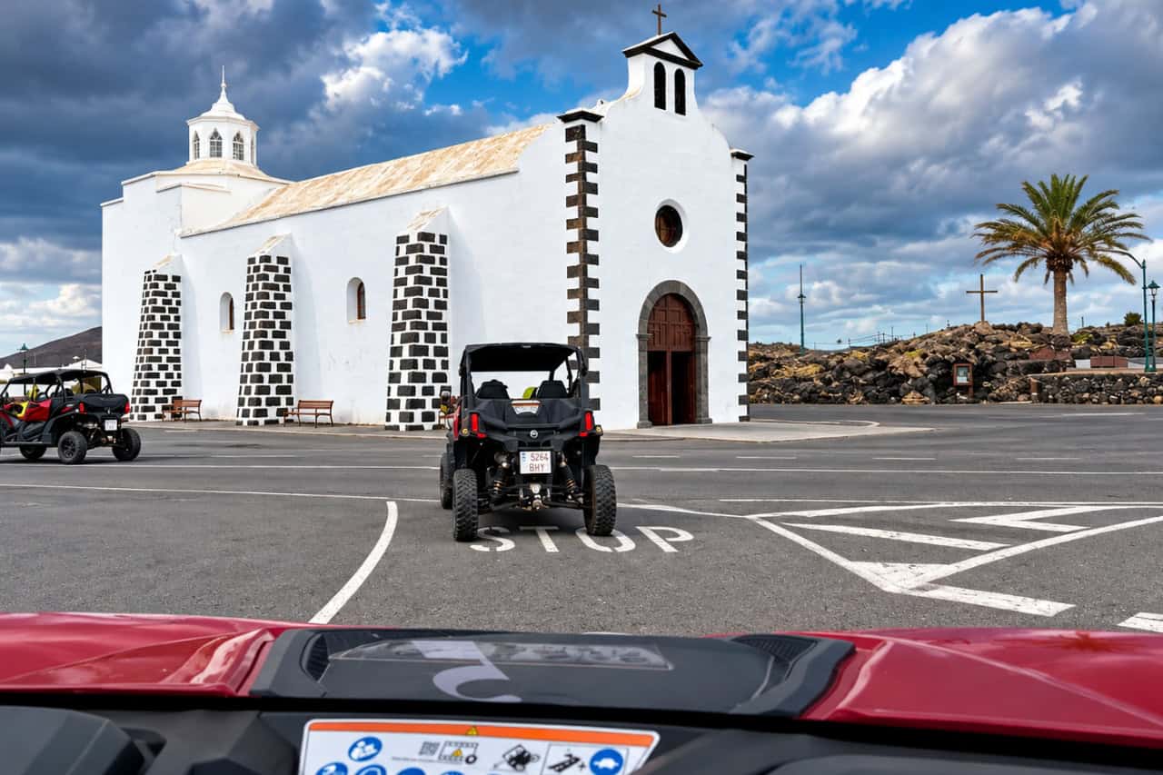 Buggy stopped beside a white Canary church with black volcanic stone in Lanzarote