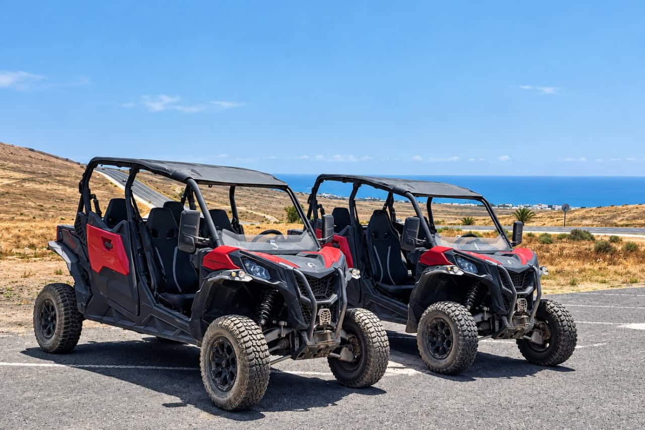 Two red four-seat buggies parked above the Lanzarote coast with the Atlantic behind