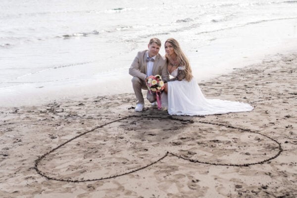 Wedding couple on the beach in Gran Canaria with bouquet inside a heart drawn in the sand