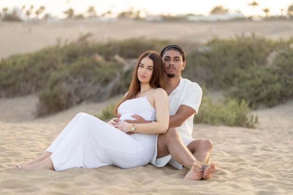 Couple sitting together in the dunes of Gran Canaria during a maternity shoot