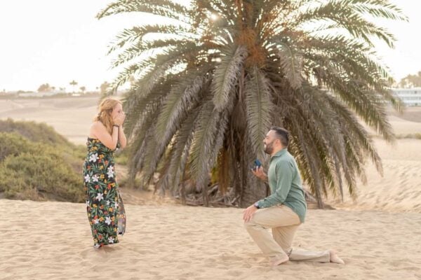 Man proposing on one knee at Maspalomas dunes in Gran Canaria, partner surprised and smiling