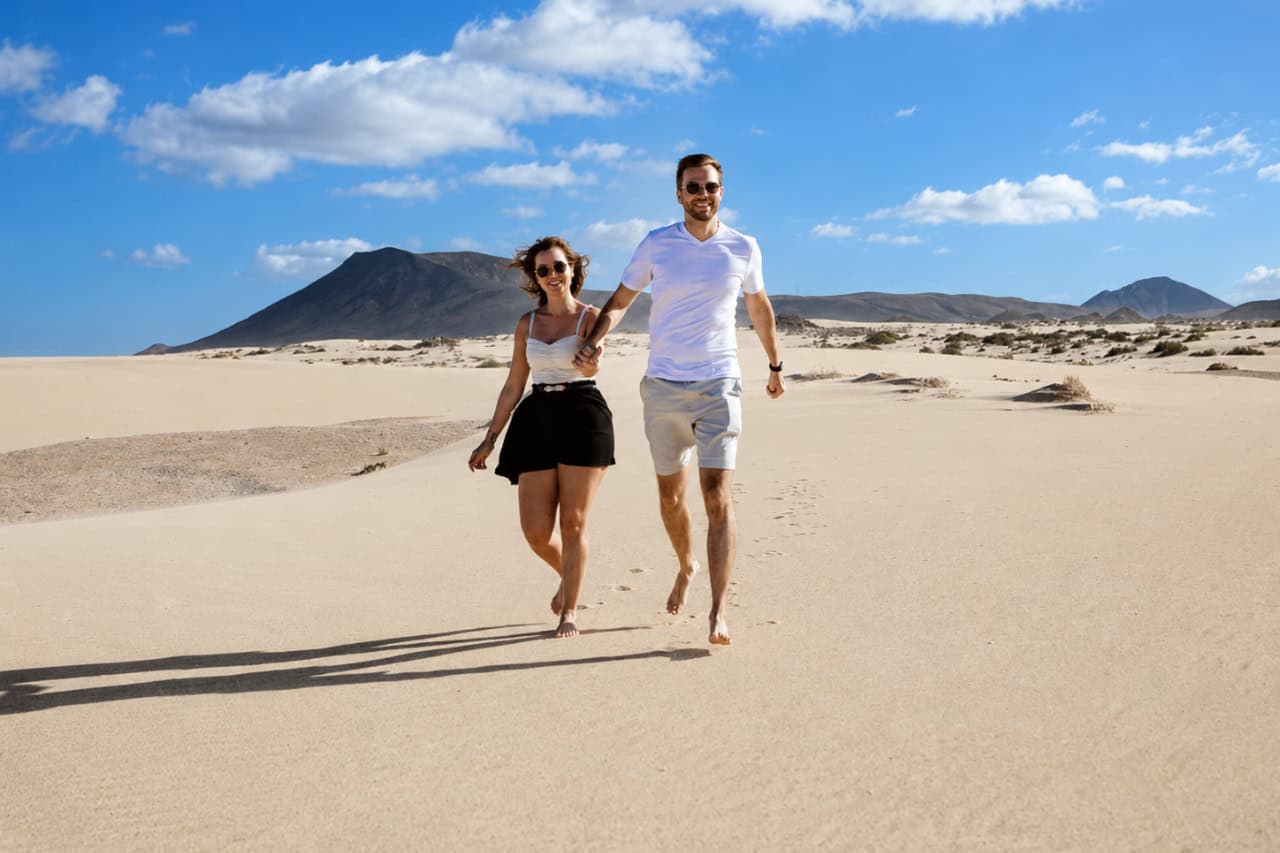 Couple running barefoot across the golden dunes of Fuerteventura