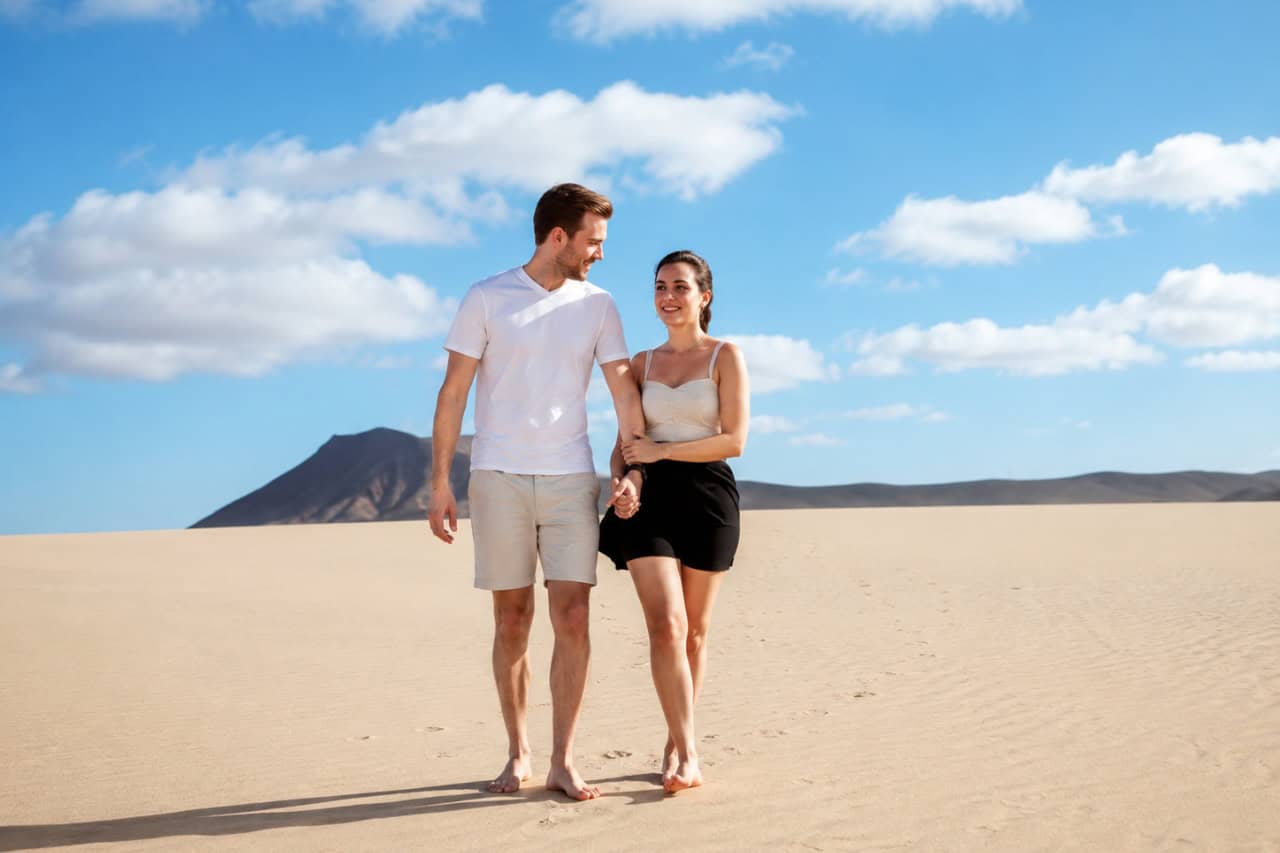 Couple walking hand in hand through the sunlit dunes of Fuerteventura
