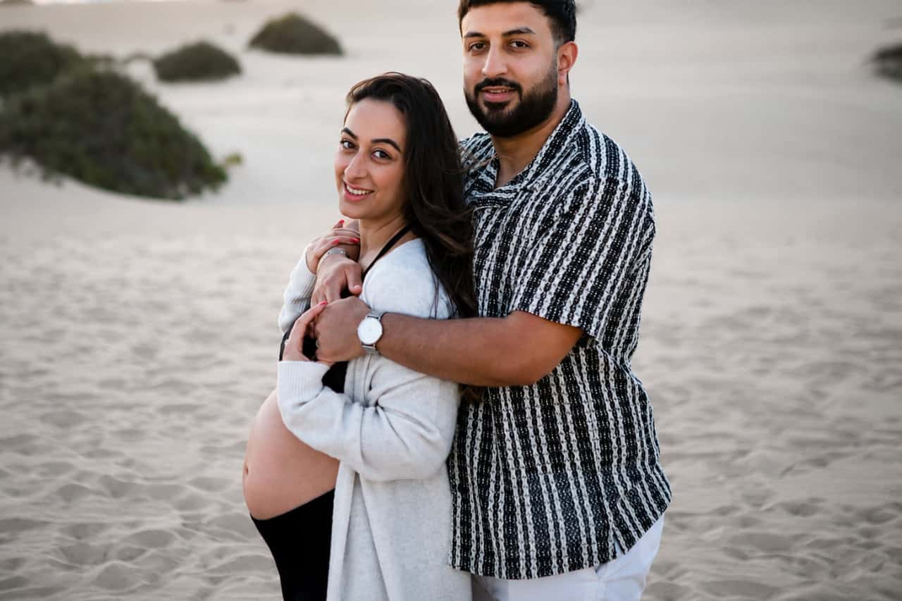 Expectant couple embracing during a maternity photoshoot in the dunes
