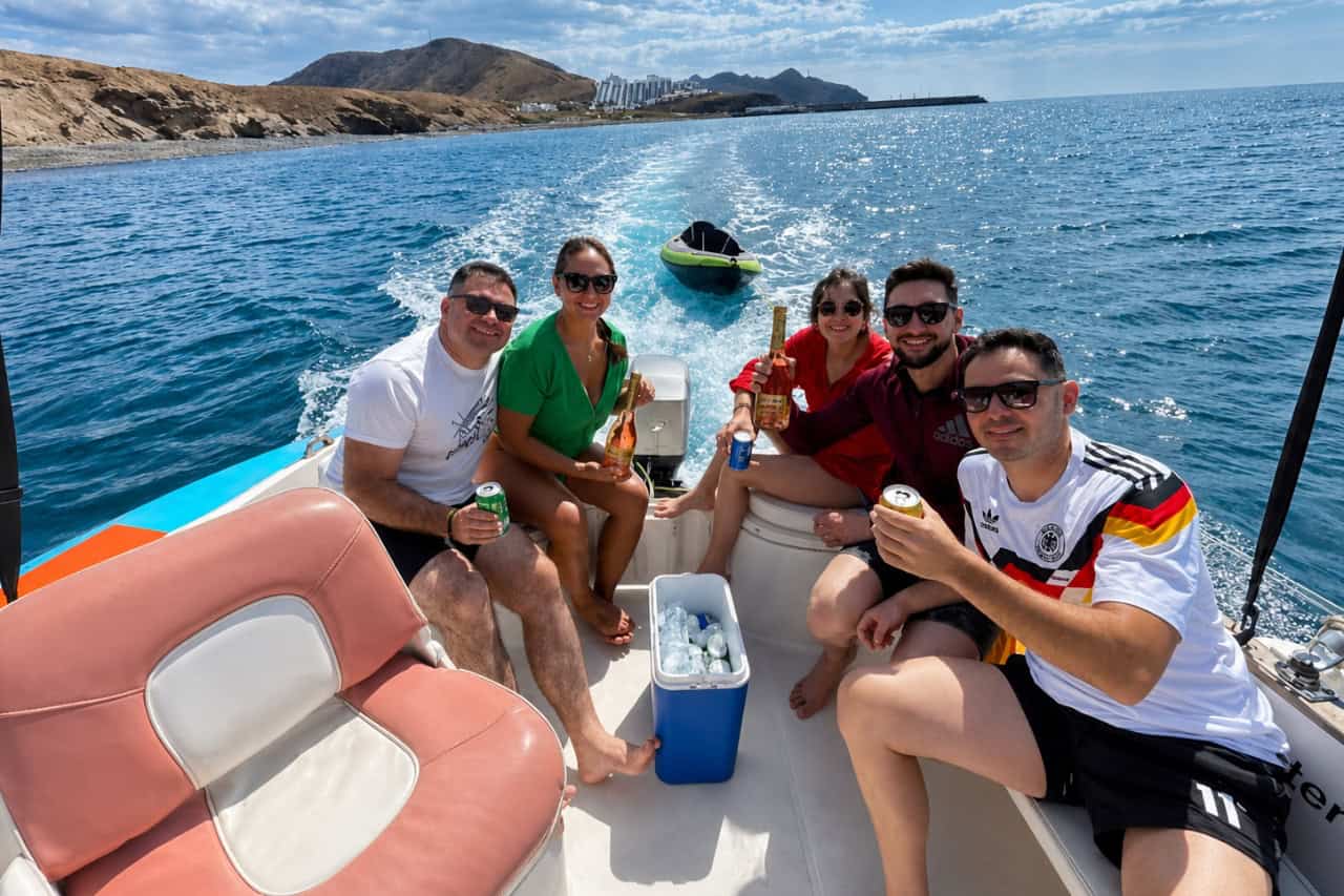 Group relaxing on a private motorboat with an inflatable kayak beside the rocky coast of Fuerteventura