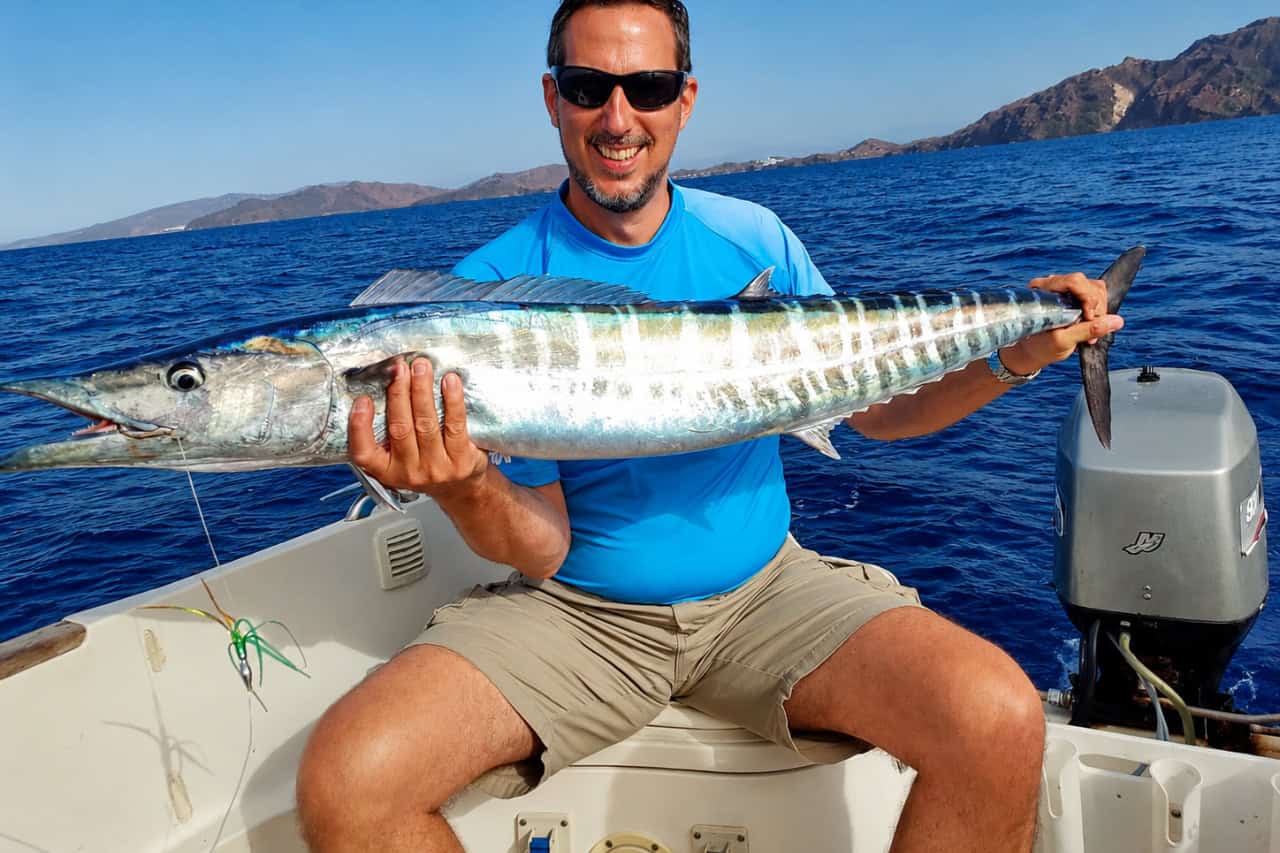 Smiling fisherman holding a large wahoo aboard a small fishing boat off Fuerteventura