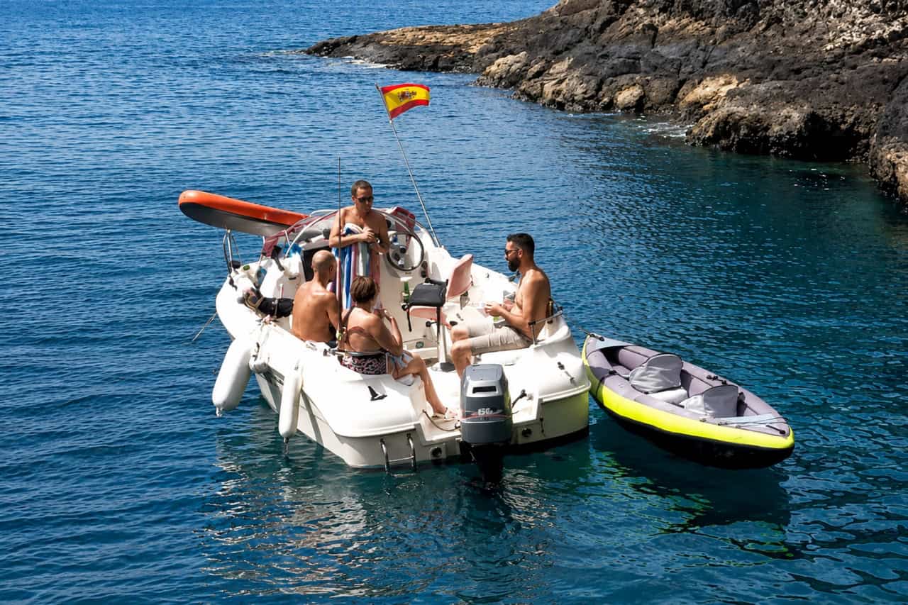 Friends enjoying drinks aboard a small boat towing an inflatable kayak along the Fuerteventura coast