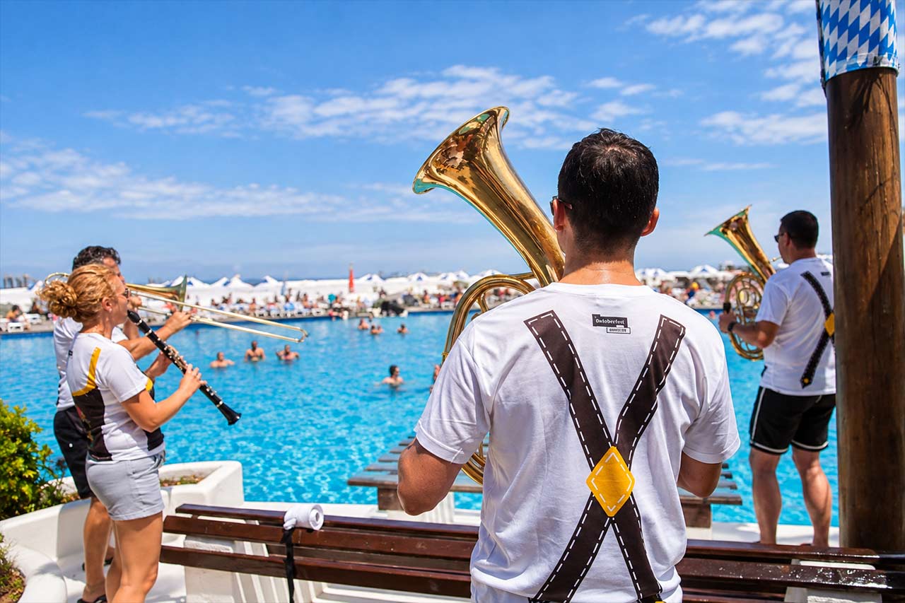 Muzicieni bavarezi cântă lângă apă în Puerto de la Cruz, reflectând atmosfera generală a Oktoberfestului din tot orașul, cu concerte live și festivități de inspirație germană.