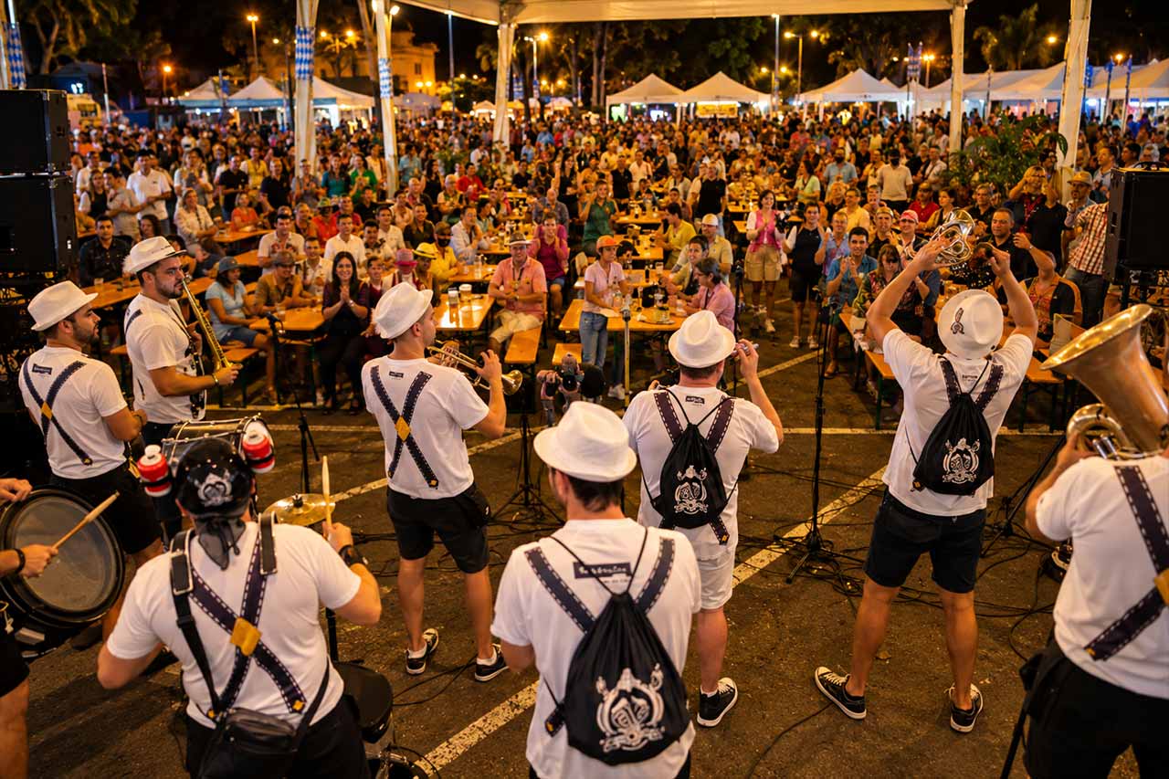 O mulțime numeroasă sărbătorește în fața formației bavareze live la Oktoberfest Puerto de la Cruz, surprinzând dansul, muzica și atmosfera plină de energie, în timp ce festivalul continuă până noaptea târziu.