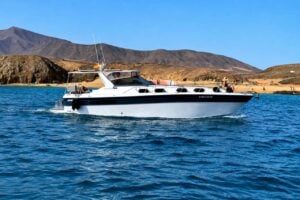 White private motor yacht cruising through blue ocean water beside the volcanic coastline of Lanzarote with no passengers visible
