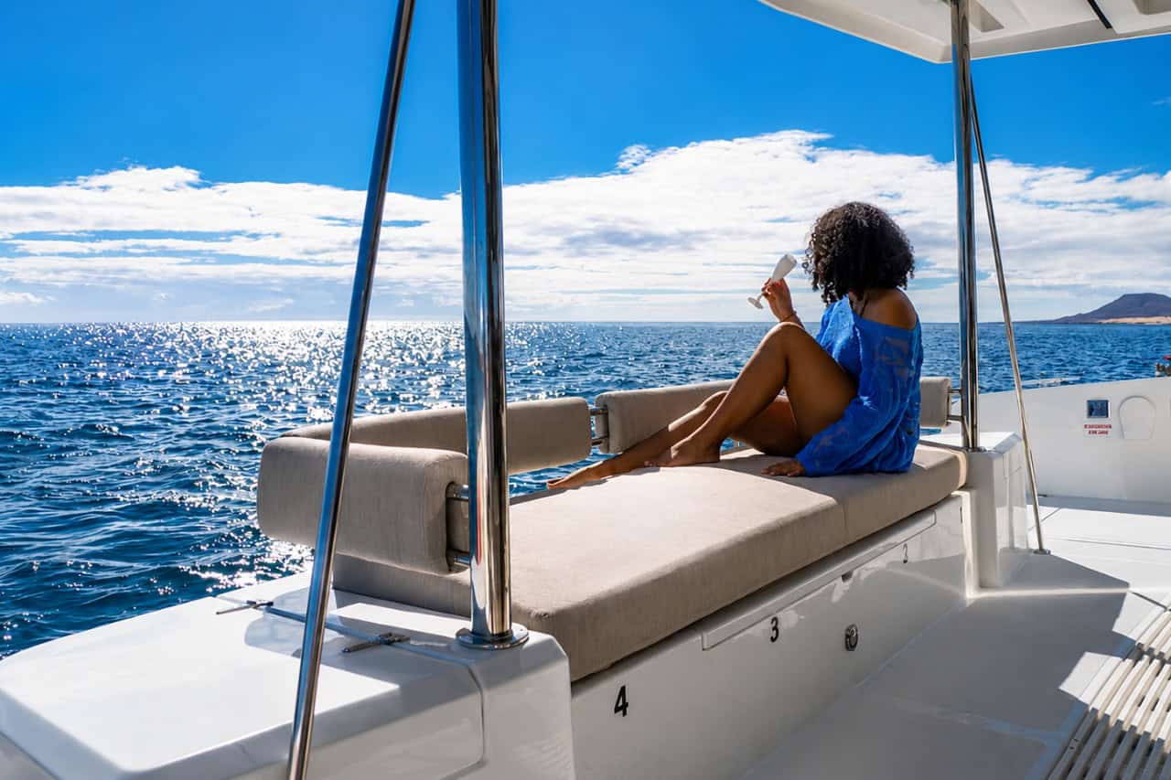 Woman relaxing with a drink on a luxury catamaran while enjoying views of the Atlantic Ocean.