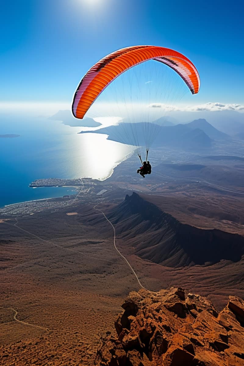 A paraglider flies in the air over the mountains, villages and ocean of the island of Lanzarote during a beautiful sunny day.