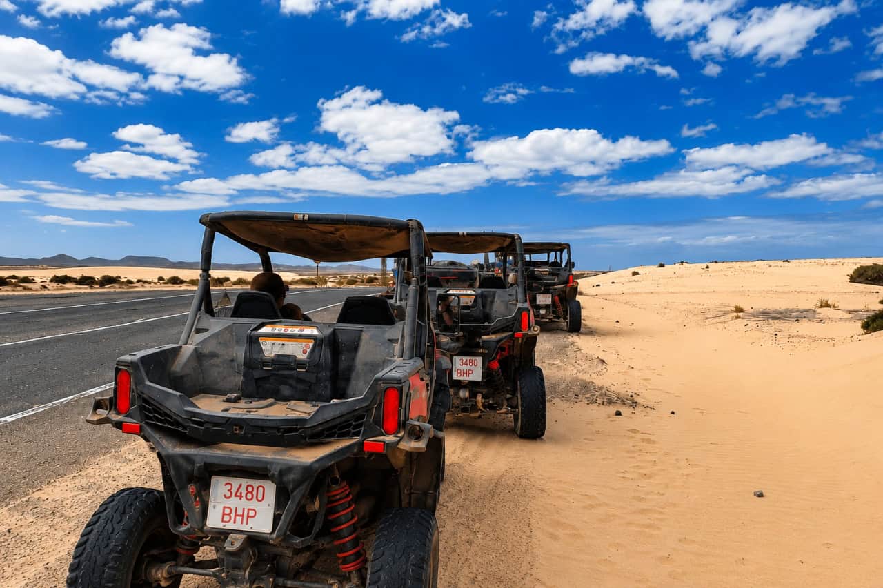 Driver’s view of a buggy convoy travelling along a sandy off-road trail beneath a bright blue sky in Fuerteventura.