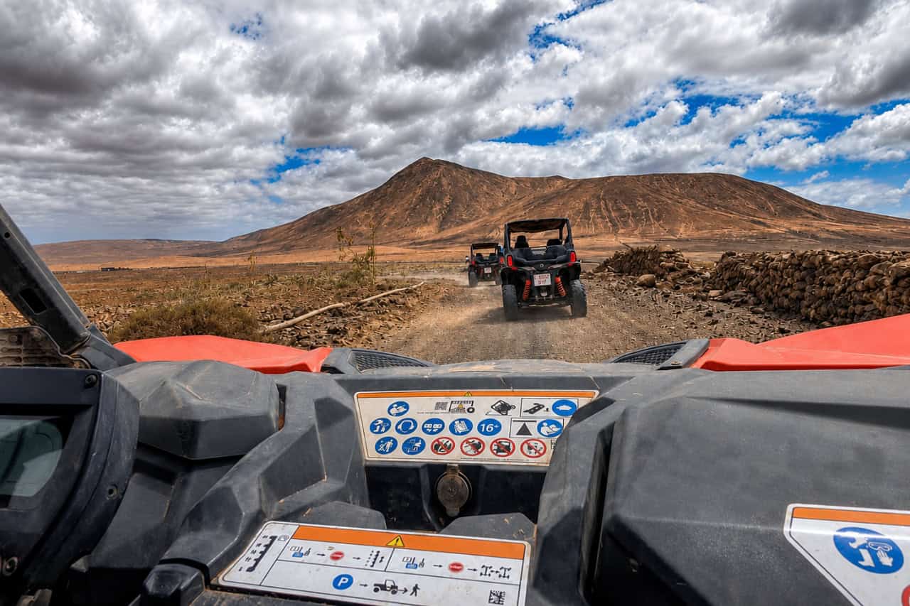 Driver’s view of a buggy convoy travelling towards a volcanic mountain under dramatic clouds in Fuerteventura.