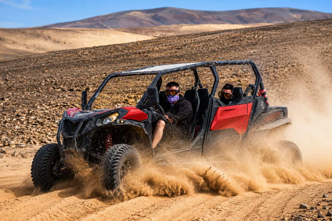 Two people riding a red off-road buggy through the volcanic landscape of Fuerteventura.