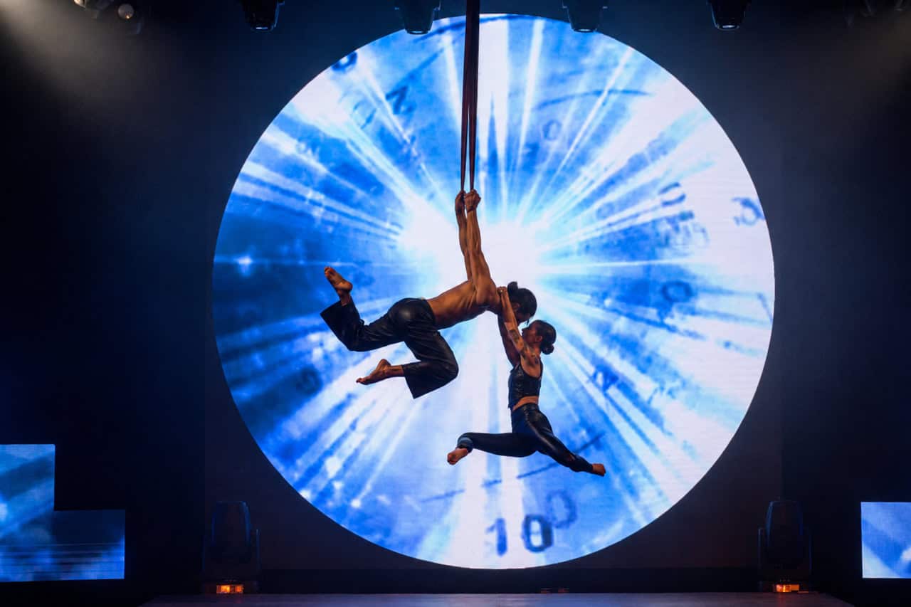 Aerial acrobats performing against a large circular screen during the History show in Tenerife