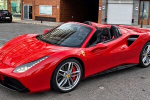 Uthyrning av röd Ferrari 488 Spider på Teneriffa visad i trefjärdedels vinkel framifrån med nedfälld cabriolet, silverfärgade lättmetallfälgar, röda bromsok, Ferrari-sköld, skulpterad motorhuven, LED-strålkastare och svart sportinteriör med röda detaljer synliga.