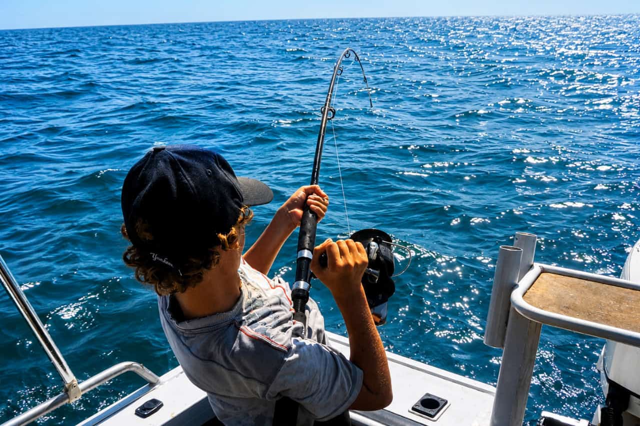 Young angler reeling in a fish from a boat during a family fishing experience in Lanzarote.