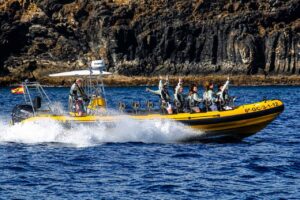 Yellow dolphin-watching speedboat cruising beside the rugged volcanic coastline of Lanzarote.