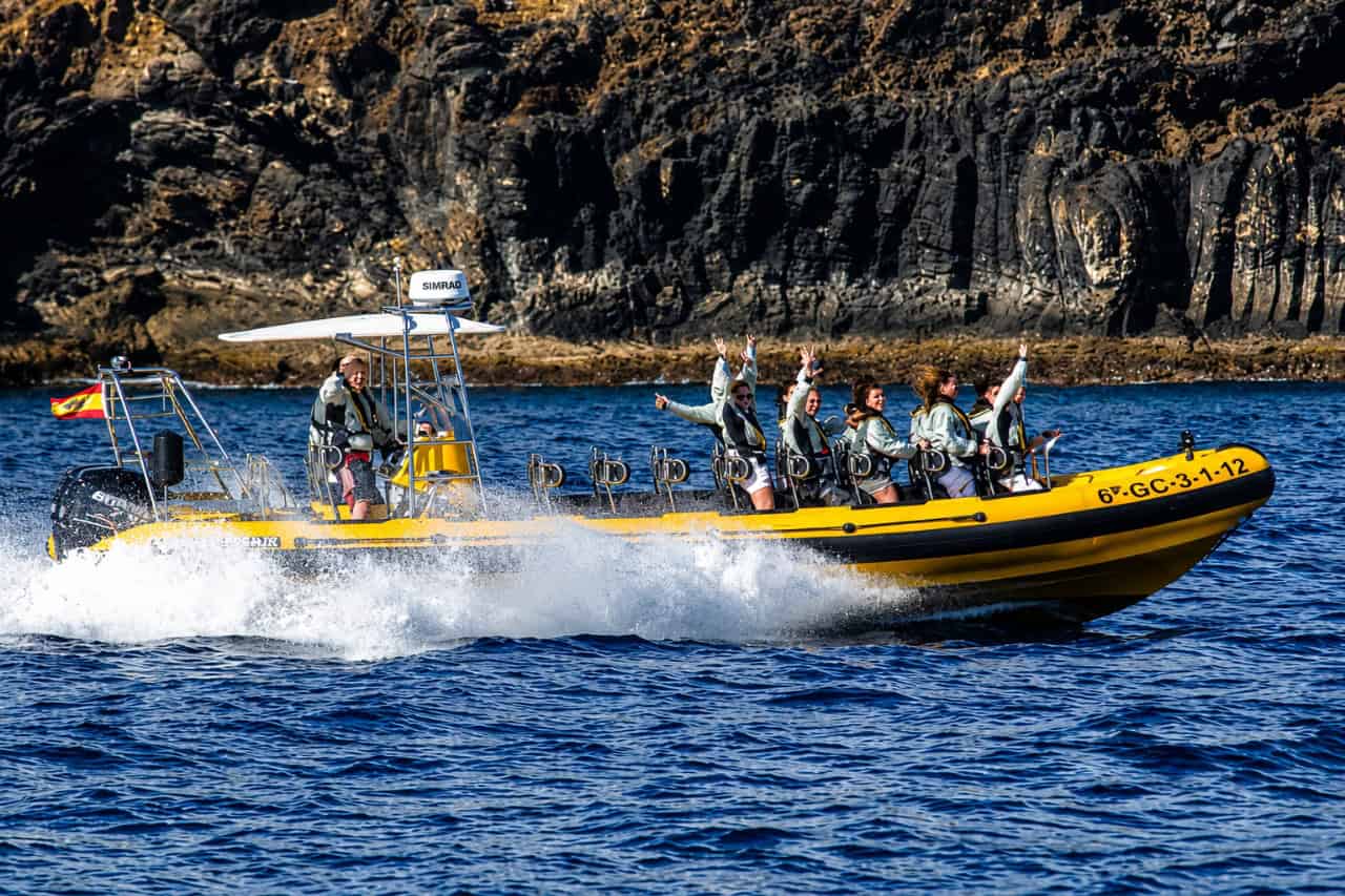 Yellow dolphin-watching speedboat cruising beside the rugged volcanic coastline of Lanzarote.