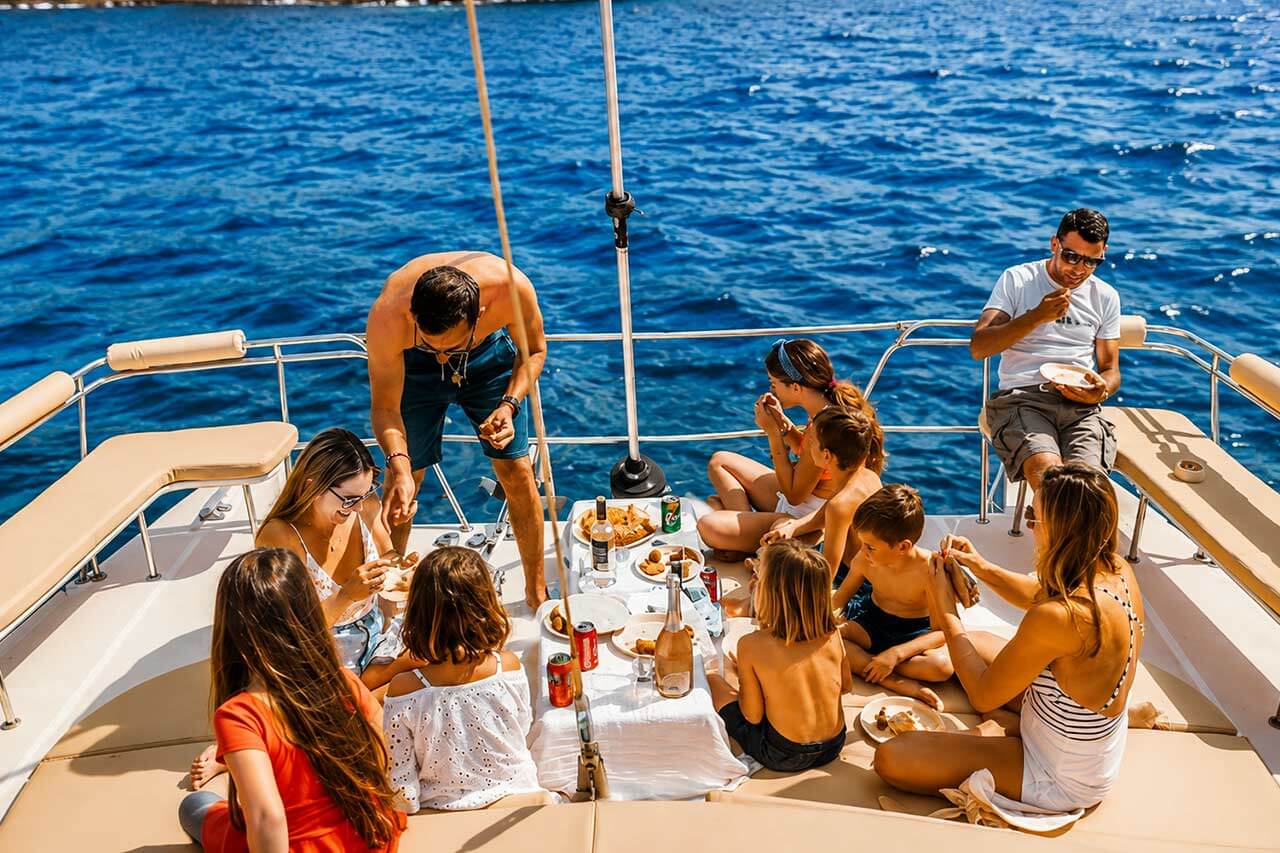 Familie en vrienden die samen eten en drinken op het ruime dek van de Kalima Kat catamaran tijdens een ontspannen boottocht op Tenerife.