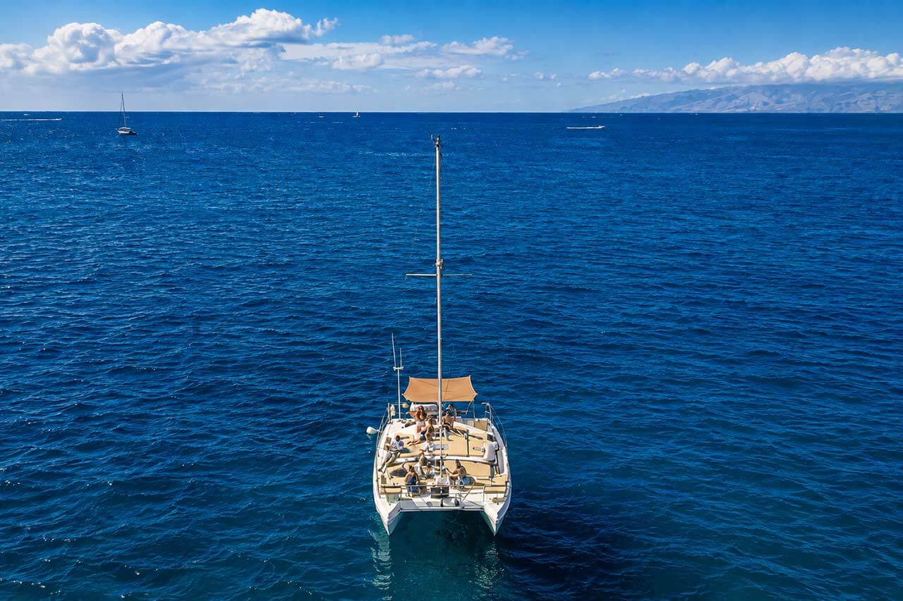 De catamaran Kalima Kat gezien van boven op open Atlantische wateren bij Tenerife, met gasten die ontspannen op het dek en de kustlijn van het eiland in de verte zichtbaar.