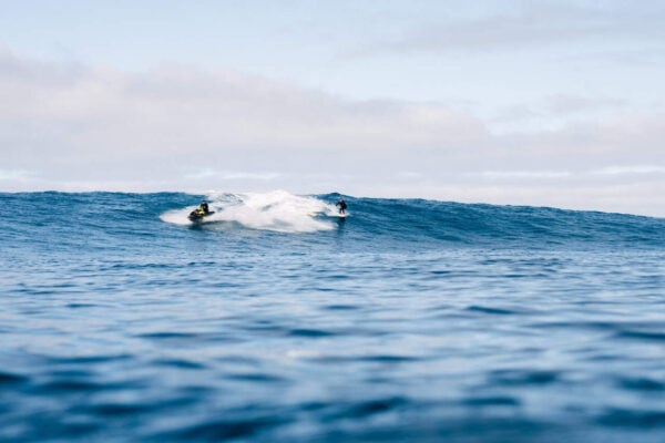 Instructor de surf pe jetski asistă un elev care călărește un val mare în timpul lecțiilor avansate de surf în Lanzarote, plaja Famara