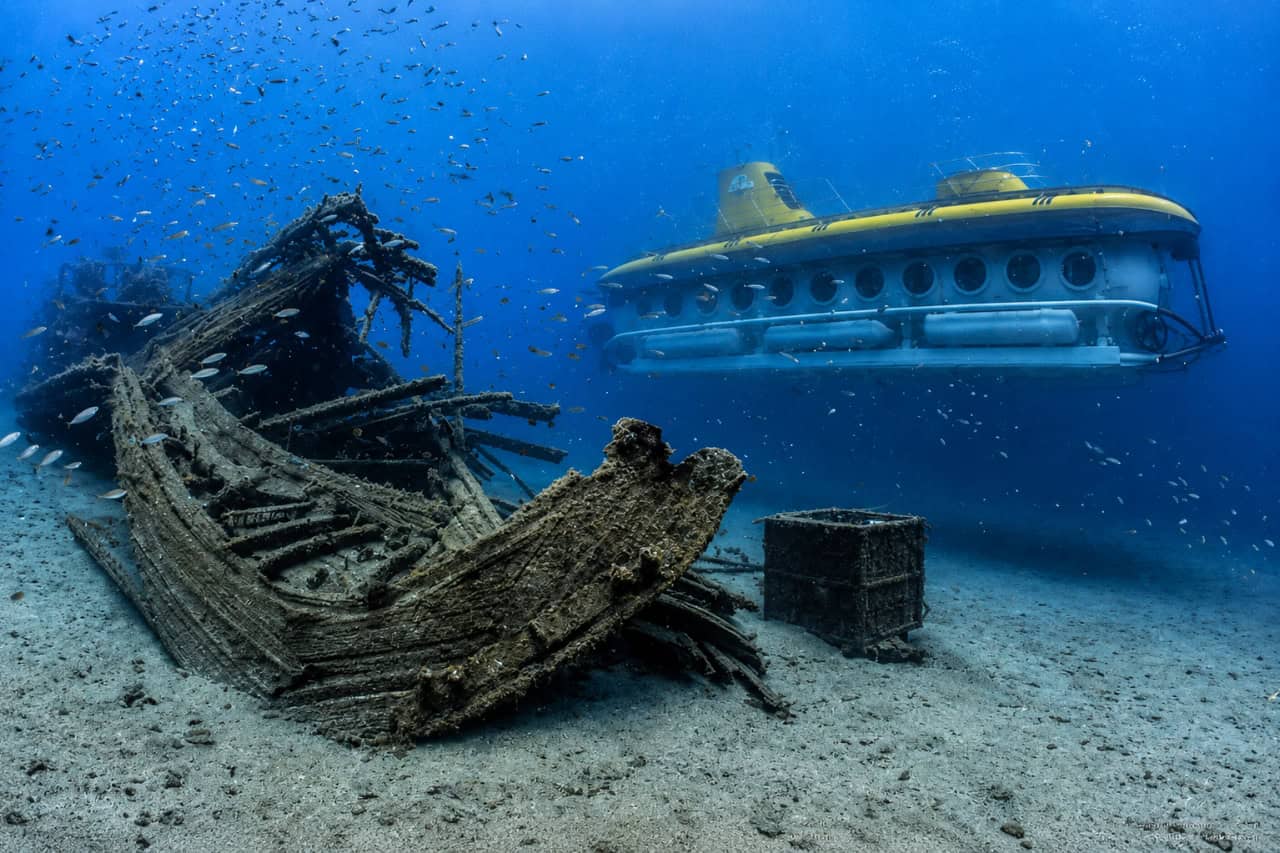 Submarine Safaris vessel cruising beside a wooden shipwreck surrounded by fish on the seabed near Lanzarote.
