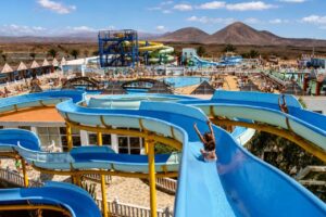 Panoramic view of a Fuerteventura water park with blue slides, swimming pools and volcanic mountains in the background.