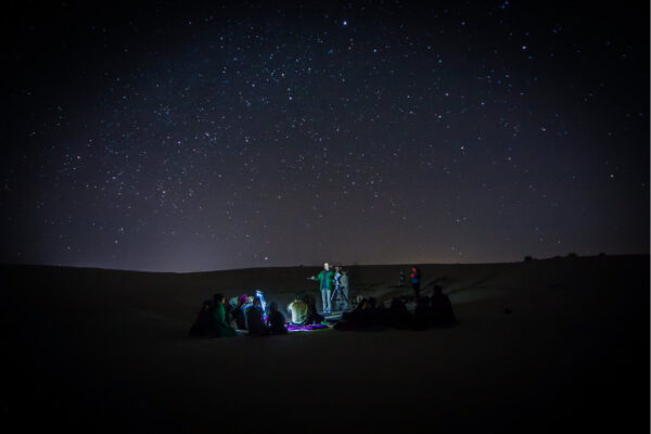 Invitados sentados en mantas durante una experiencia guiada de observación de estrellas en Fuerteventura con telescopio y cielo nocturno por encima.