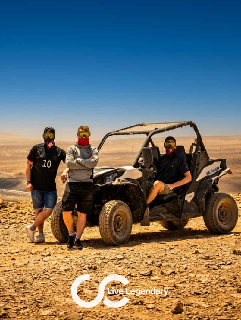 Three friends with goggles and face scarves posing by a Can-Am buggy in the Fuerteventura desert