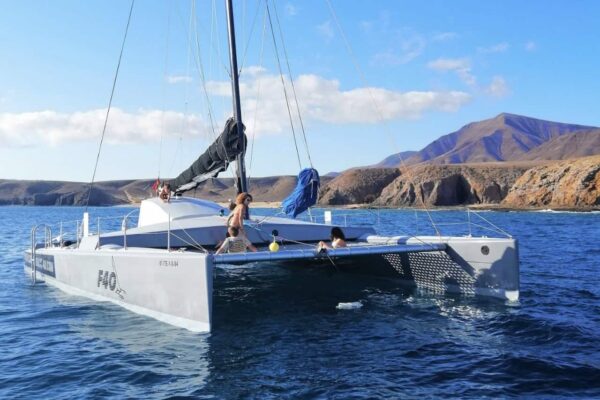 F40 sailing catamaran anchored in clear blue water near the cliffs and beaches of Playa Blanca, Lanzarote