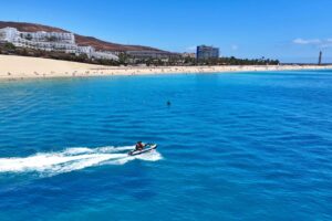 Solo rider on a jet ski speeding across the bay at Morro Jable with the beach and lighthouse behind on a Fuerteventura jet ski rental
