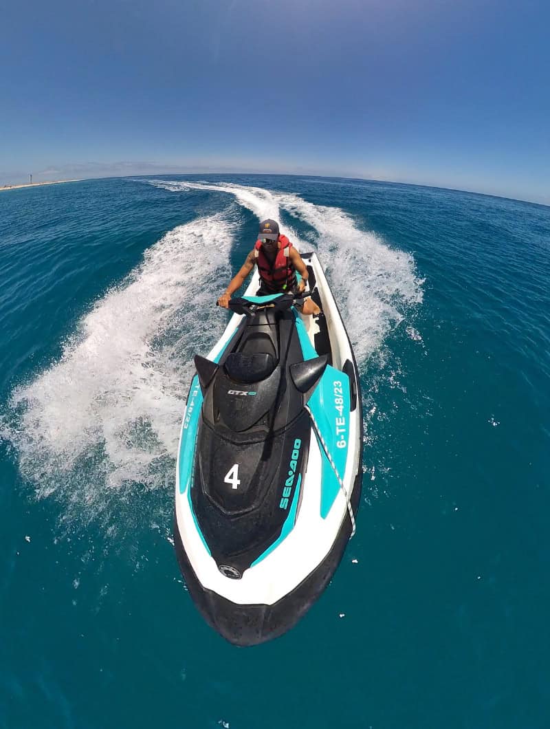 Vandens motociklu Sea-Doo važiuojantis motociklininkas skrieja virš skaidraus mėlyno vandens palei Morro Jable pakrantę Fuerteventuroje