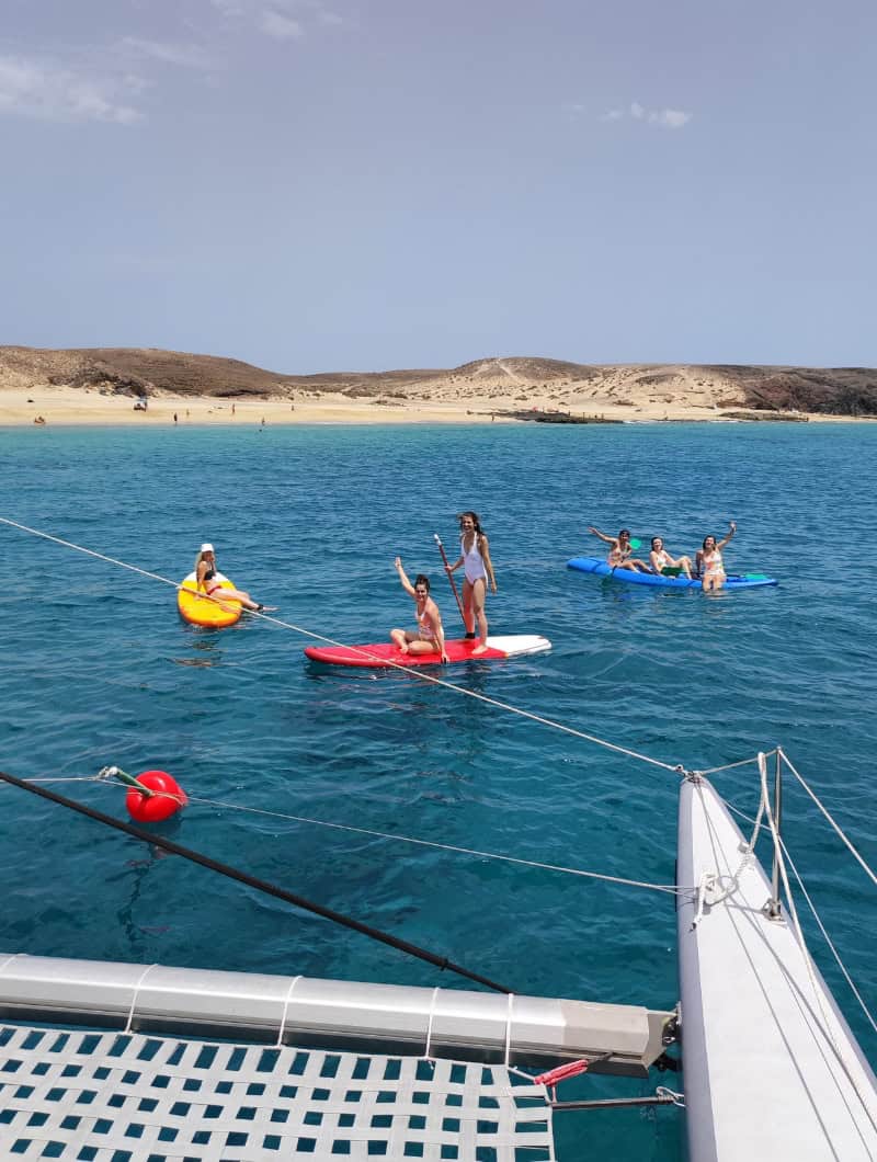 Groep vrienden die lachen op paddleboards en kajaks in turquoise water bij Papagayo tijdens een privé catamarancruise op Lanzarote