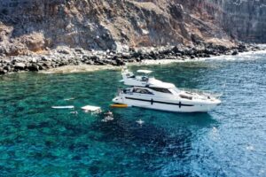 Die Blue M Yacht ankert in einer klaren Bucht, während Gäste auf einem privaten Charter in der Nähe von Puerto de Mogán, Gran Canaria, schwimmen und Stand-Up-Paddling betreiben.