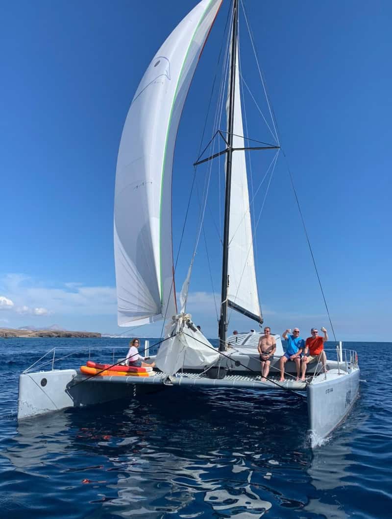 Vrienden die ontspannen en hun drankjes heffen op de trampoline van de F40 catamaran tijdens het zeilen voor de kust van Lanzarote