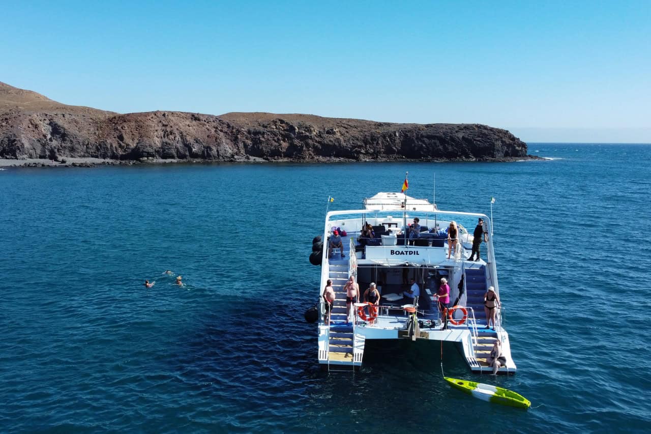 Guests swimming from a private catamaran anchored at a quiet bay on the Fuerteventura south coast