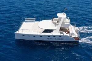 Aerial view of a white 14-metre luxury catamaran cruising across the deep blue waters off the coast of Tenerife, available for private charter.
