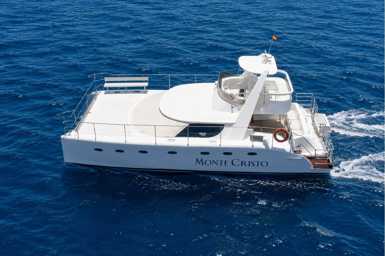 Aerial view of a white 14-metre luxury catamaran cruising across the deep blue waters off the coast of Tenerife, available for private charter.