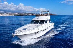 Luxury white motor yacht cruising along the Tenerife coastline on a sunny day, offering a private yacht charter experience on the Atlantic Ocean.