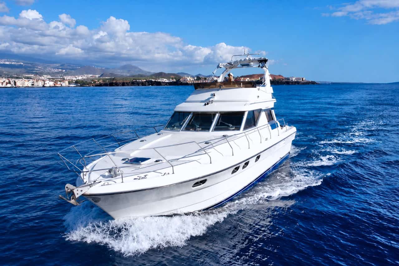 Luxury white motor yacht cruising along the Tenerife coastline on a sunny day, offering a private yacht charter experience on the Atlantic Ocean.