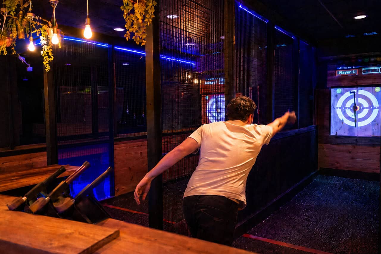 Person throwing an axe at a wooden target inside a modern indoor axe throwing venue in Tenerife, featuring neon lighting and enclosed throwing lanes.