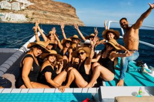 Group of guests enjoying the sun and celebrating on the front deck of the Freebird catamaran during a boat trip along Tenerife's southwest coast near the cliffs of Costa Adeje.