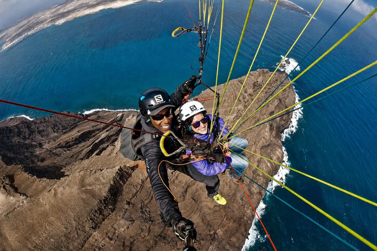 Tandem paragliding couple flying high above Lanzarote’s rocky coastline and deep blue Atlantic Ocean during an adventurous aerial experience.