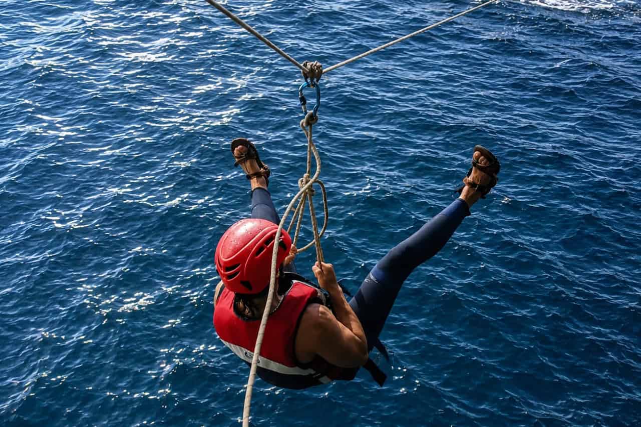 Person in a red helmet and life jacket lowering down a rope into the deep blue sea on a coasteering tour in Gran Canaria