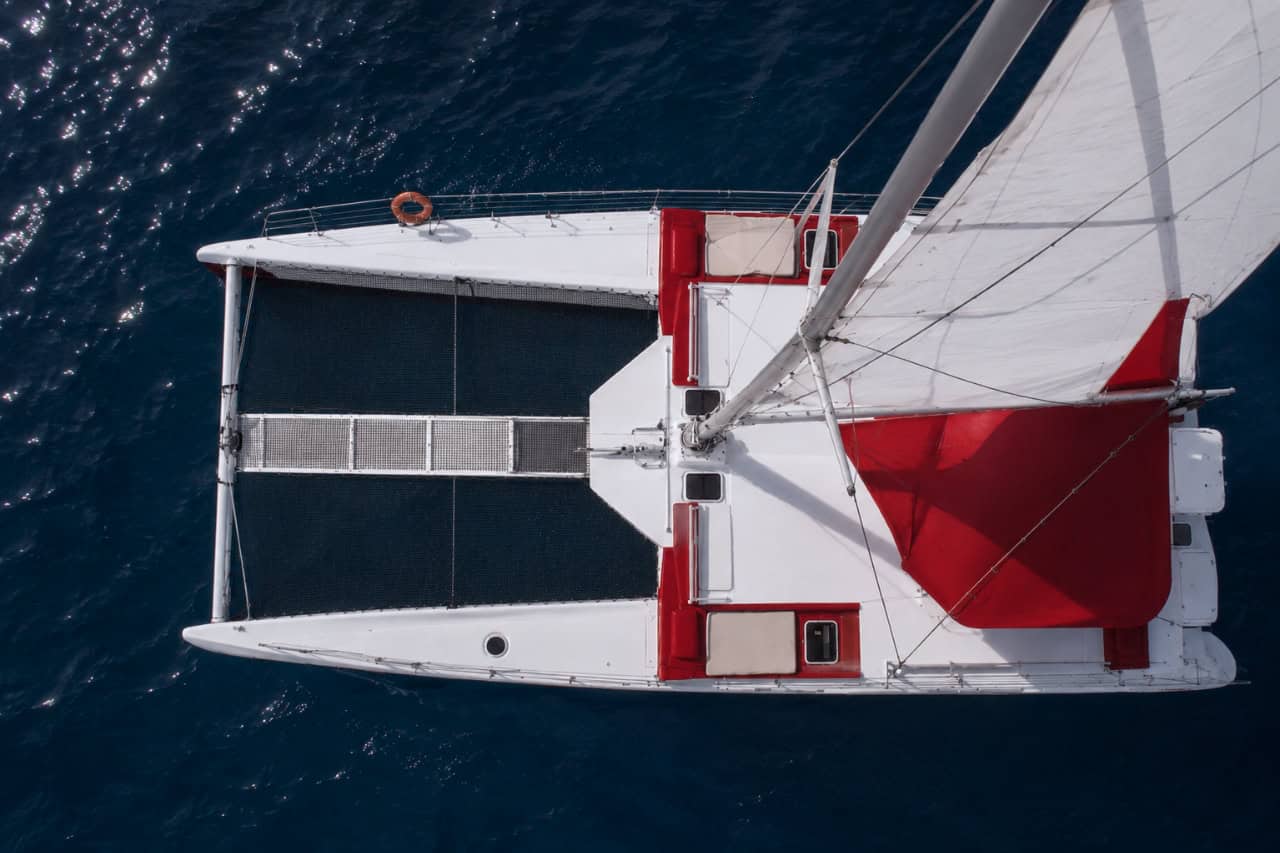 Top-down aerial view of an eco-friendly red and white catamaran sailing in the deep blue Atlantic Ocean off Tenerife, featuring spacious decks and a modern solar-assisted design.